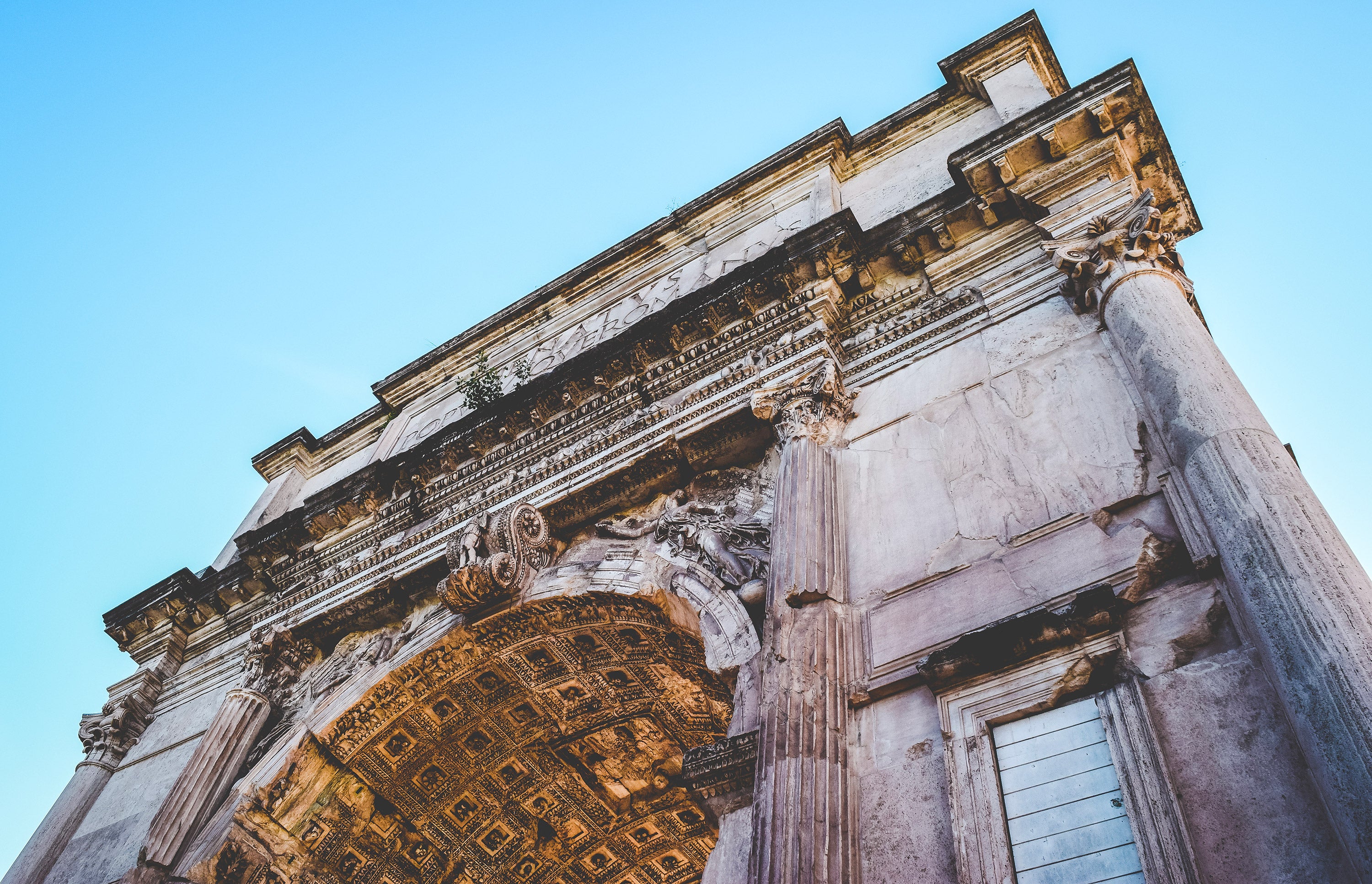 Architectural detail of a classical building with intricate carvings against a clear blue sky.